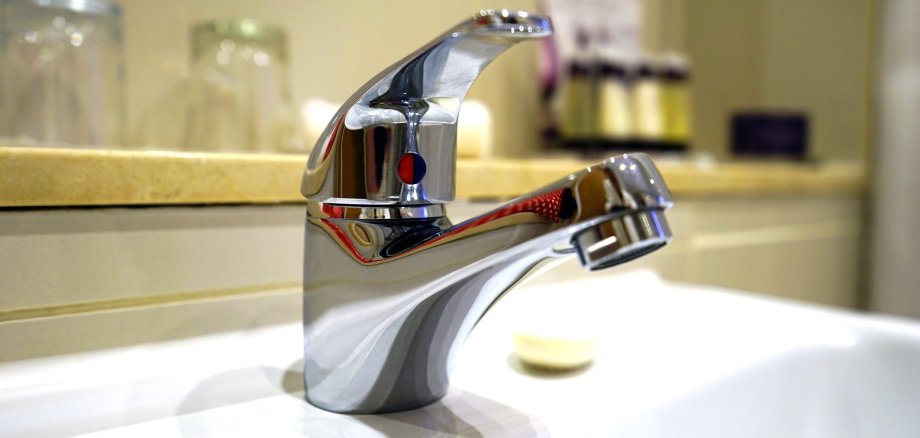 Wasserhahn mit Trinkgläsern im Hintergrund