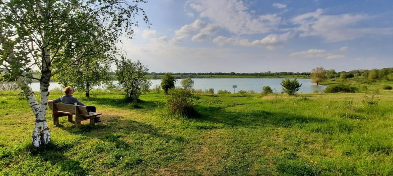 Ein Mann sitzt auf einer Bank und blickt auf den Bergwerksee