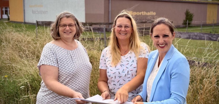 Bauamtsleiterin Petra Klöppel, Kita-Leiterin Corina Morkel und Bürgermeisterin Lena Herget stehen auf dem Baugrundstück der neuen Kita in Reichelsheim